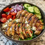 A close-up view of a vibrant Greek chicken bowl topped with fresh vegetables and feta cheese.