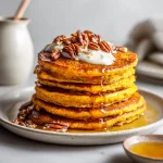 A stack of fluffy sweet potato pancakes topped with syrup and warm, soft light illuminating their texture.