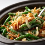 Close-up of a creamy green bean casserole topped with crispy fried onions, lit by soft natural light.