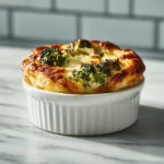 Close-up of a creamy broccoli casserole topped with crushed crackers, illuminated by warm natural light.