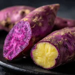 Close-up of two baked Japanese sweet potatoes with a golden-brown skin, resting on a rustic wooden surface.