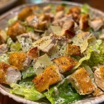 A close-up side view of a Low Carb Caesar Salad with grilled chicken, garnished with parmesan crisps.