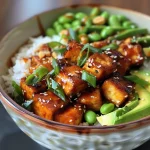 Close-up of a bowl filled with sticky tofu, rice, edamame, and avocado.