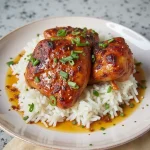 Close-up of juicy chicken thighs glazed in a sticky sauce, garnished with green onions.