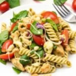 Close-up of a vibrant Chicken Pesto Pasta Salad featuring rotini pasta, cherry tomatoes, and mozzarella.