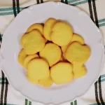 Close-up of buttery cookies stacked on a wooden table, showing their golden-brown texture.
