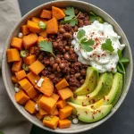 Close-up of a Sweet Potato Taco Bowl filled with diced sweet potatoes, black beans, corn, avocado, cherry tomatoes, and red onion.