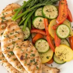 Close-up of grilled garlic and herb chicken with colorful veggies.