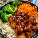 A close-up view of a teriyaki chicken rice bowl featuring tender chicken, brown rice, steamed broccoli, and colorful carrots, beautifully arranged and garnished with green onions and sesame seeds.