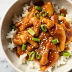 Close-up view of Slow Cooker Honey Garlic Chicken with a glossy sauce, garnished with green onions.