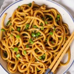 Close-up of vegan garlic noodles with garlic and green onions, presented in a rustic bowl.