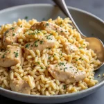 Close-up of a creamy chicken and rice dish in a bowl, garnished with parsley.