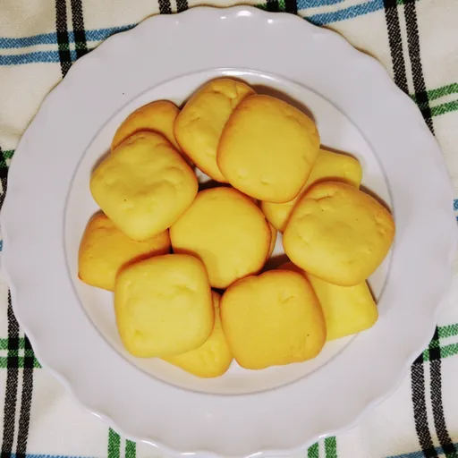 A plate of freshly baked butter cookies, glistening in natural light with soft shadows highlighting their shape.