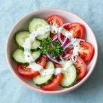 A fresh and creamy cucumber tomato salad served in a white bowl