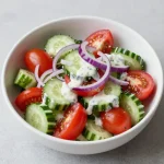 A vibrant creamy cucumber tomato salad served in a bowl with fresh herbs