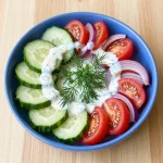 A fresh creamy cucumber tomato salad served in a bowl with a sprinkle of herbs on top
