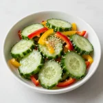 A colorful bowl of cucumber pepper salad topped with fresh herbs