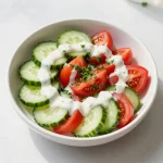 A vibrant creamy tomato cucumber salad in a bowl garnished with fresh herbs