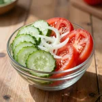 A vibrant bowl of marinated cucumbers, onions, and tomatoes garnished with herbs