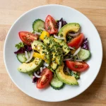 A vibrant summer salad featuring cherry tomatoes, cucumber, avocado, red onions, and basil pesto.