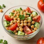 A vibrant chickpea salad with diced tomatoes and cucumbers on a wooden table