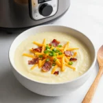 A bowl of creamy potato soup garnished with chives and served with crusty bread
