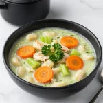 A bowl of creamy chicken gnocchi soup garnished with fresh herbs
