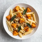 A creamy butternut squash pastasotto topped with fresh herbs and grated cheese