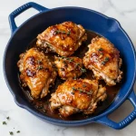 A plate of braised chicken thighs garnished with apple slices and herbs